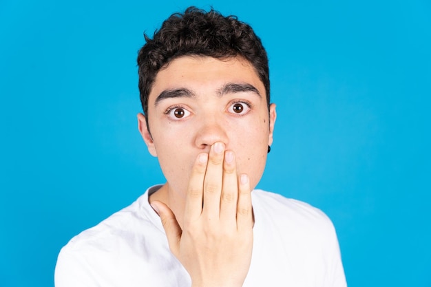 Retrato de un adolescente hispano sorprendido con la mano en la boca y mirando a la cámara