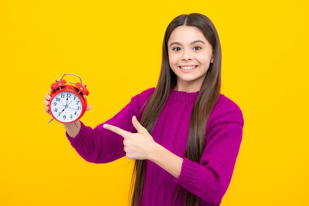 Retrato de una adolescente con la hora de la alarma del reloj y la fecha límite Foto de estudio aislada sobre fondo amarillo