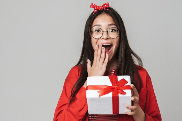 Foto retrato de una adolescente joven emocionada conmocionada aislada sobre la pared gris que sostiene la caja de regalo actual.