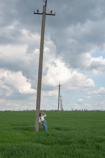 Retrato de una adolescente de moda posando junto a un pilar en un paisaje rural de campo de hierba verde en jeans