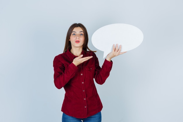 Foto retrato de una adolescente mostrando bocadillo en camisa burdeos y mirando sorprendido vista frontal