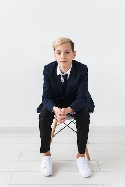 Retrato de adolescente de niño de escuela elegante en camisa blanca y chaqueta contra la pared blanca con espacio de copia