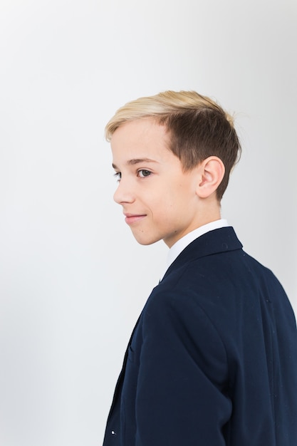 Retrato de adolescente de niño de escuela con estilo en camisa blanca y chaqueta contra la superficie blanca.