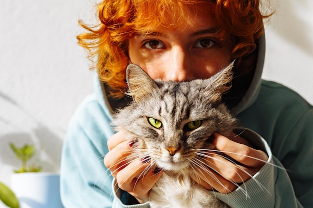 Retrato de una adolescente pelirroja con un gato de pelo verde esponjoso