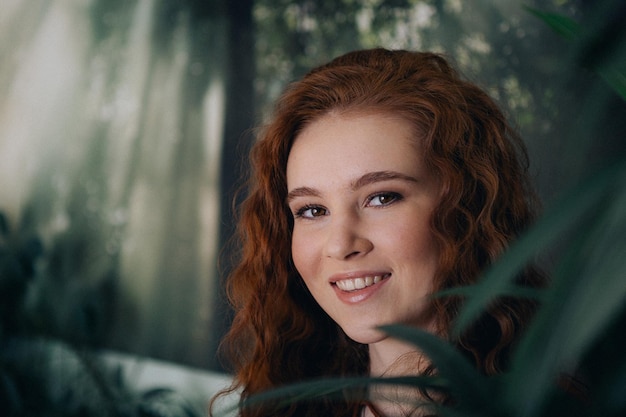 Foto retrato de una adolescente pelirroja con el pelo rizado sobre un fondo de plantas verdes