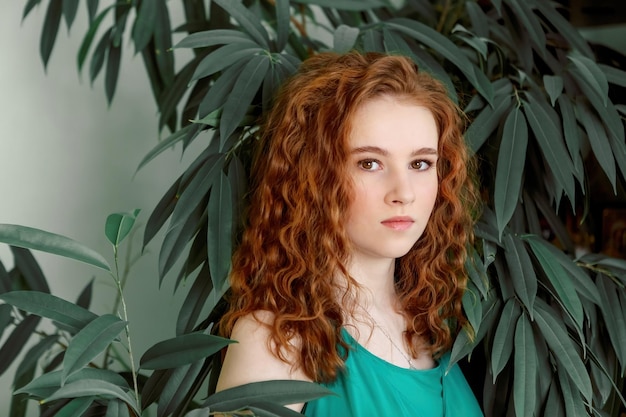 Foto retrato de una adolescente pelirroja con el pelo rizado sobre un fondo de plantas verdes