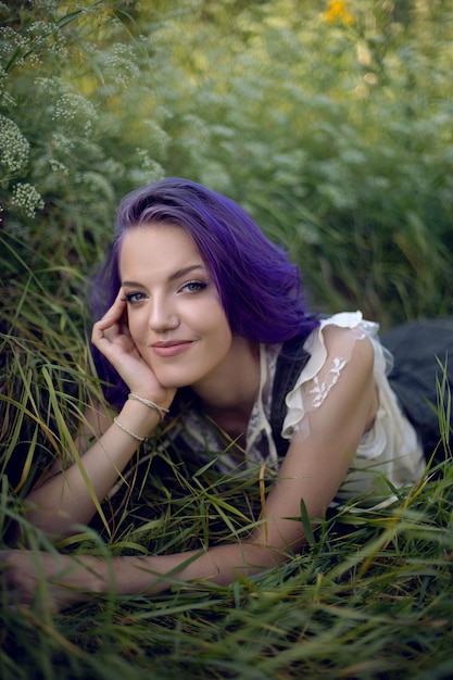 Retrato de una adolescente con el pelo morado y un pendiente en la nariz tumbado en la hierba en la naturaleza