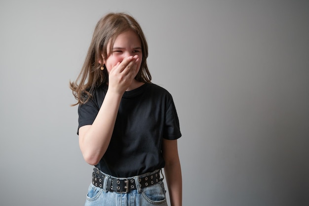 Retrato de una adolescente que cubre su rostro con las manos sobre fondo gris Foto de alta calidad