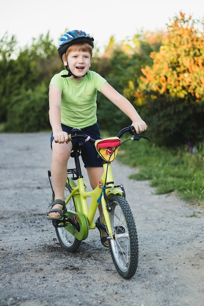 Foto retrato de un adolescente riéndose con casco y camiseta verde montando bicicleta en verano en la carretera