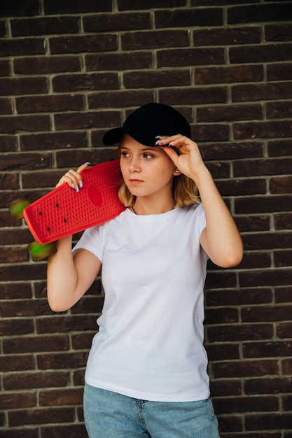 Retrato de una adolescente con ropa informal contra una pared de ladrillos Estilo de vida activo de skate de verano Un estudiante o un estudiante en vacaciones de verano Actividades deportivas