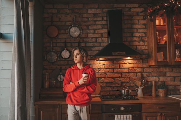 Retrato de un adolescente sincero y auténtico soñador que disfruta de una taza de café caliente por la mañana en casa Navidad