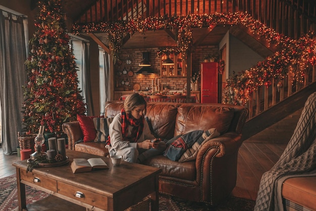 Retrato de un adolescente sincero, auténtico y sonriente que usa un teléfono móvil en el interior de la casa de Navidad