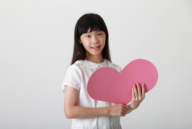 Retrato de una adolescente sonriente con forma de corazón mientras está de pie contra un fondo blanco