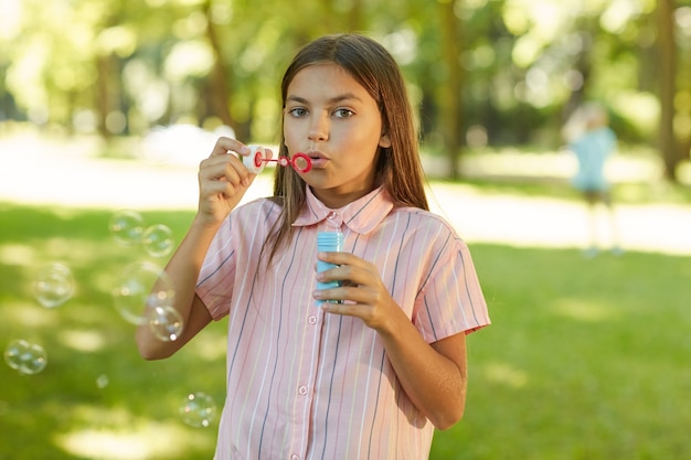 Retrato de una adolescente soplando burbujas mientras está de pie en el parque verde al aire libre