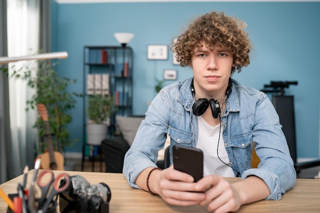 Retrato de adolescente usando un teléfono inteligente y sonriendo en el escritorio en la sala de estar en casa