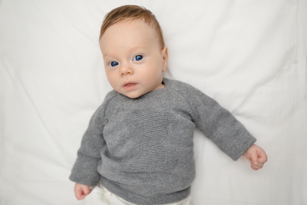 Retrato de adorable bebé con ojos azules acostado en la cama Bebé sonriendo y mirando a la cámara