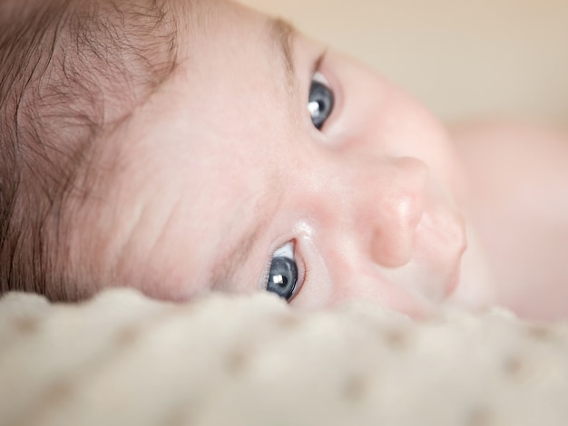 Foto retrato de adorable bebé recién nacido con los ojos abiertos acostado sobre una manta