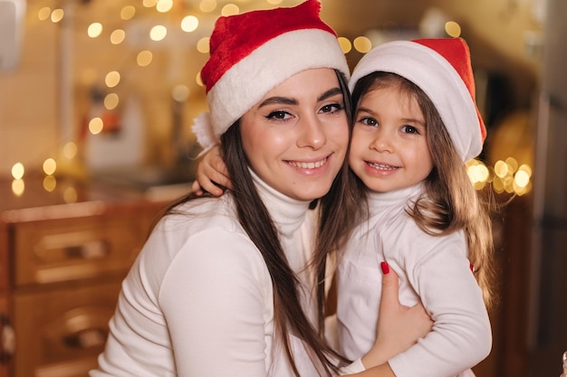 Retrato de adorable hijita con su mamá en la cocina durante las vacaciones de Navidad decorativas