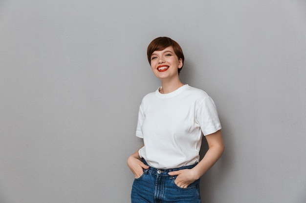 Retrato de adorable mujer morena vistiendo camiseta casual sonriendo al frente aislado sobre pared gris