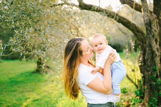 Retrato de una adorable niña en brazos de su madre debajo de un olivo