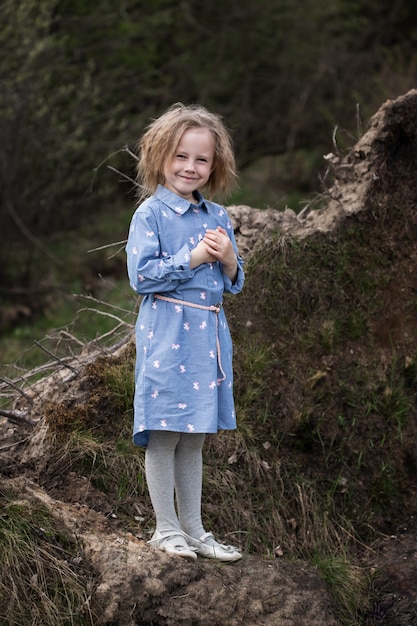 Retrato de adorable niña caucásica de 5 años de pie en el bosque y mirando a la cámara