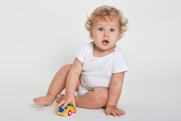 Retrato de adorable niño sentado en el suelo descalzo y vestidos traje de cuerpo