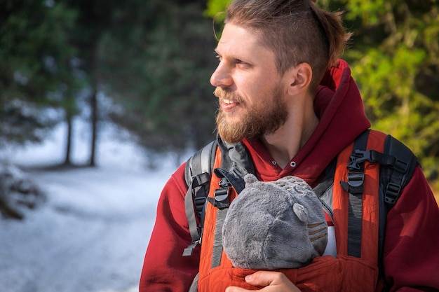 Retrato de adorable padre portador de bebé barbudo con su hijo en un portabebés de invierno al aire libre