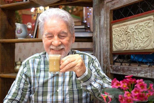 Retrato de un adulto maduro y sonriente abuelo barbudo sentado en el interior sosteniendo una taza de café