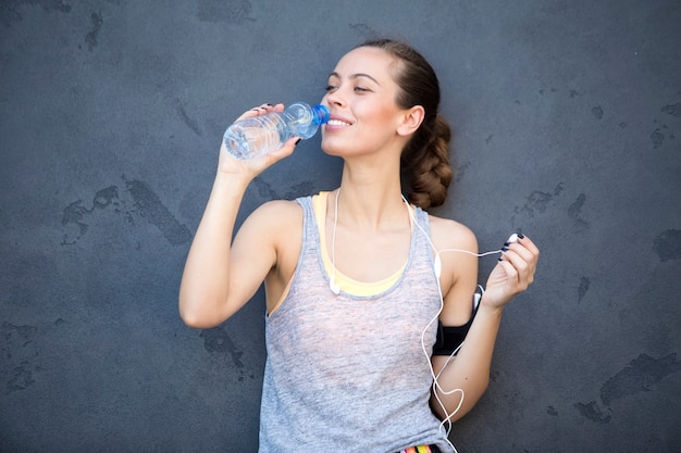 Foto retrato del agua potable de la mujer atlética joven por la pared