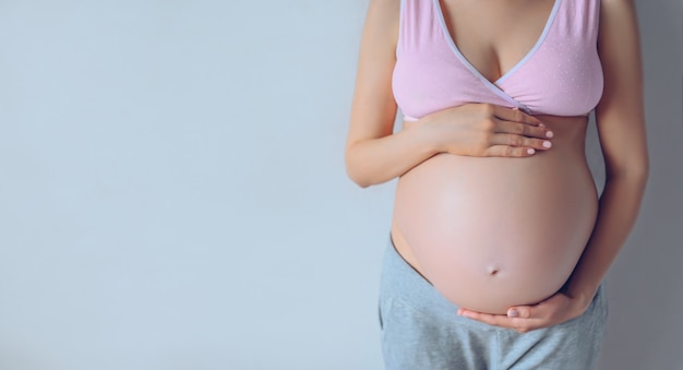 Retrato aislado de mujer embarazada irreconocible tomados de la mano sobre su gran barriga con bebé dentro. Concepto de embarazo, maternidad, nonato y expectativa. Copia gratis