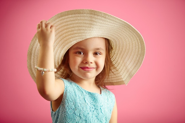 Retrato aislado de niña con sombrero de panamá sonrisa sostiene soportes de sombrero de mano en rosa aislado