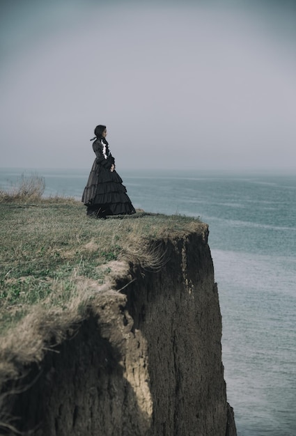 Retrato al aire libre de una dama victoriana vestida de negro parada en el acantilado