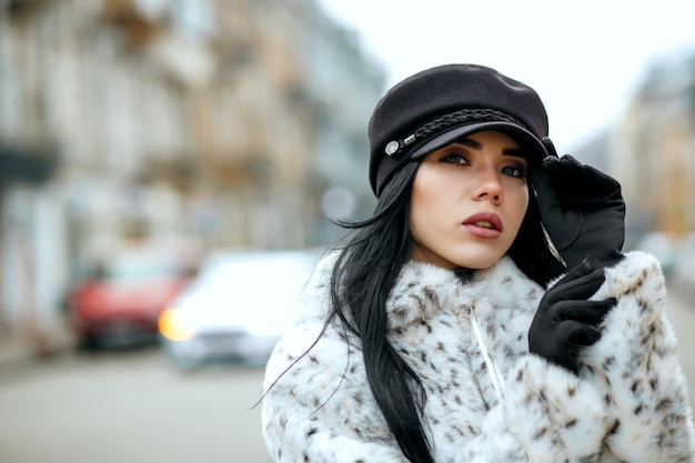 Retrato al aire libre de una elegante mujer morena con elegante gorra y abrigo. Espacio para texto