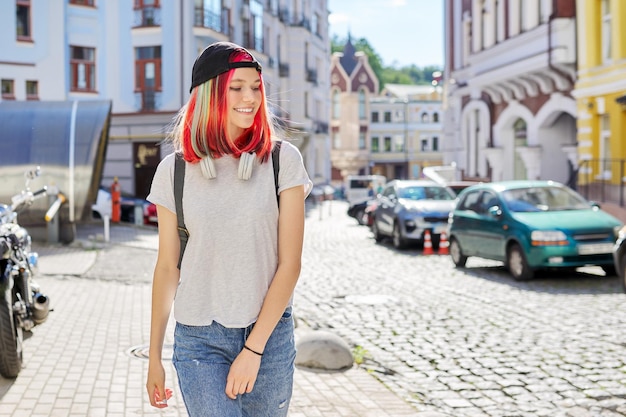 Retrato al aire libre de una estudiante adolescente sonriente con gorra negra con mochila, mujer de moda con el pelo teñido de color en la calle de la ciudad, espacio para copiar. Estilo de vida, juventud, moda, belleza, gente joven.