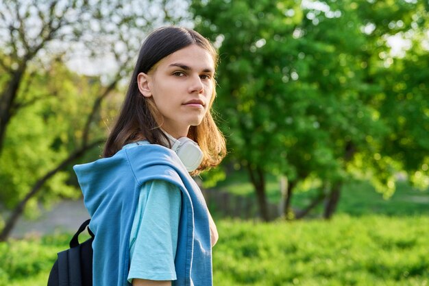 Retrato al aire libre de un estudiante guapo con mochila mirando la cámara fondo del campus del parque verde Joven hombre sonriente con espacio de copia de peinado de pelo largo Concepto de jóvenes de educación juvenil