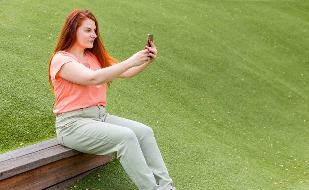 Retrato al aire libre de la hermosa chica de jengibre tomando un selfie