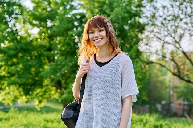 Retrato al aire libre de una hermosa estudiante adolescente sonriente con mochila mirando a la cámara chica pelirroja positiva de 18 años de edad green park campus de fondo juventud educación de belleza jóvenes