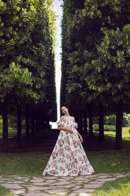 Retrato al aire libre de una hermosa mujer morena de lujo con un vestido con flores en un parque con árboles recortados