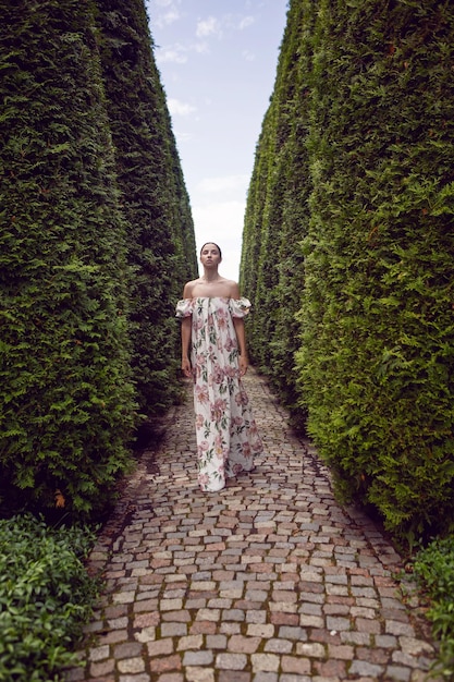Retrato al aire libre de una hermosa mujer morena de lujo con un vestido con flores en un parque con árboles recortados