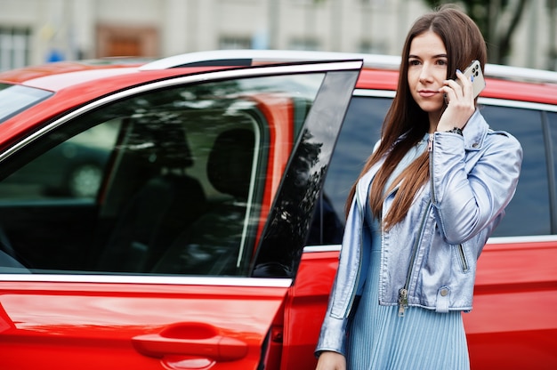 Retrato al aire libre de hermosa mujer posando junto a suv naranja con puerta abierta, habla por teléfono