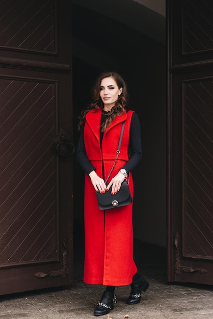 Foto retrato al aire libre de una joven elegante en la calle de una ciudad vieja vestida de negro y un chaleco rojo largo una modelo posa en la calle de una ciudad europea