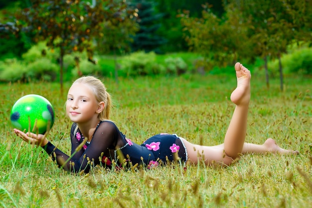 Retrato al aire libre de joven gimnasta niña linda formación con pelota sobre el césped