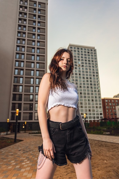 Retrato al aire libre de una joven hermosa mujer en pantalones cortos y top posando contra el fondo de la ciudad