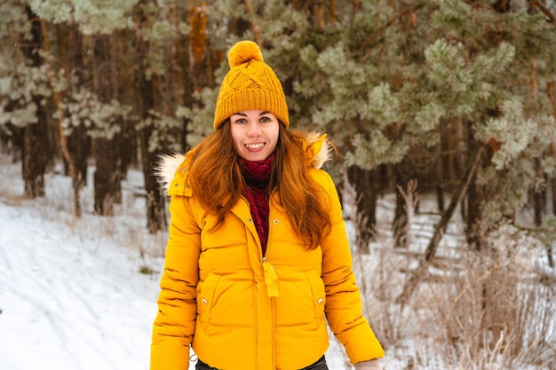 Retrato al aire libre de una joven mujer sonriente con una chaqueta amarilla, caminando en el bosque de invierno