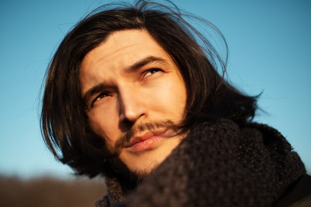 Retrato al aire libre de joven pensativo con cabello largo sobre fondo de cielo azul