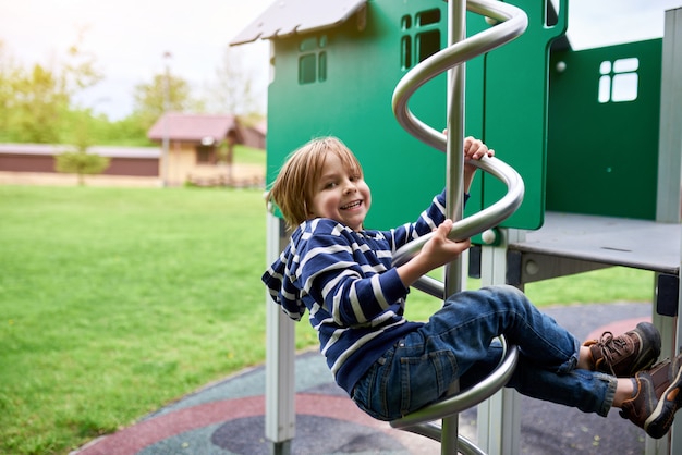 Retrato al aire libre de lindo niño preescolar escalada en el patio de recreo