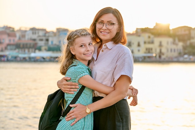 Retrato al aire libre de mamá e hija de 10 a 11 años en el paseo marítimo de la ciudad al atardecer