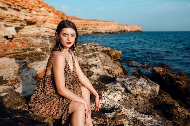 Retrato al aire libre de moda de una mujer sexy hermosa y elegante con el pelo largo vestida con un lujoso vestido de noche posando en la playa de verano