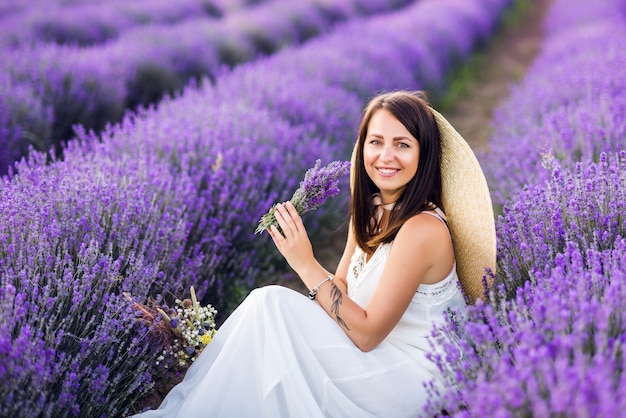 Retrato al aire libre de la muchacha adolescente joven hermosa. Morena con sombrero con cesta de flores cosechando en campo de lavanda Provenza, al atardecer. Chica guapa atractiva con el pelo largo.