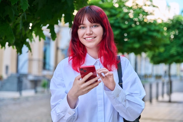 Retrato al aire libre de mujer adolescente con teléfono inteligente en las manos mirando a la cámara en la ciudad